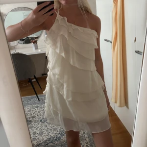 Vit omlottklänning med volanger - Säljer en jätte söt vit kortklänning med volanger och oneshoulder-design. storlek S❤️❤️