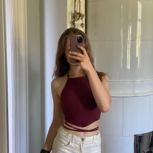 Vinröd croppad halterneck-topp med snörning - Säljer en vinröd croppad halterneck-topp med snygg snörning i ryggen. Toppen har en tight passform och är perfekt för sommaren. Materialet känns mjukt och stretchigt och är tunns men inte genomskinligt.