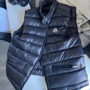 Moncler Väst - Tja! Köpte denna av en polare utan att testa den då vi nästan är lika långa och det visade sig att den var lite för liten för mig:(                     Testade den på några polare och den passade bäst mellan 170-185! Västen är äkta och tagg funkar, bild på etiketter osv finns! Västen är en size 2 och Byte mot likadan väst fast i size 3-4 är intressant eller annan väst i M-L