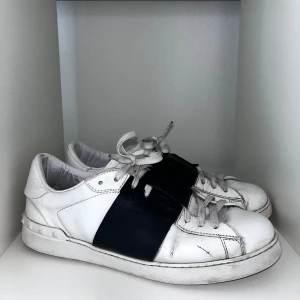 Valentino skor - Säljer ett par vita Valentino Open sneakers med bred svart rem över mitten. Skorna har snörning, rund tå och platt sula. Storlek 44, allt og ingår, skick 7/10, pris går att diskutera✅