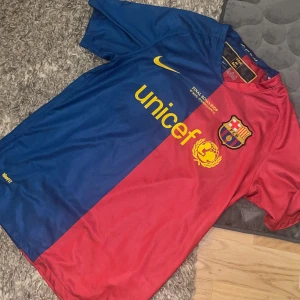 FC Barcelona matchtröja Nike - Säljer en klassisk FC Barcelona 08/09 fotbollströja från Nike med Dri-Fit material. Tröjan är kortärmad och har Barcelonas ikoniska blå och röda färger med gul Nike-logga och Unicef-tryck på bröstet. Perfekt för fans av fotbollen!