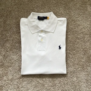 Vit pikétröja från Polo Ralph Lauren - Klassisk vit pikétröja från Polo Ralph Lauren med broderad marinblå logga på bröstet. Storlek L. Tröjan är i mycket bra skick och har varit väl omhändertagen. Pris kan diskuteras vid snabb affär!