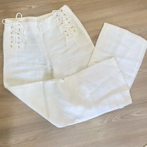 Vita linnebyxor med snörning från KappAhl - Säljer ett par vita linnebyxor från KappAhl med snygg snörningsdetalj i midjan. Byxorna har raka ben och hög midja, vilket ger en stilren och luftig känsla. Perfekta för varmare dagar och enkel att matcha med olika toppar.