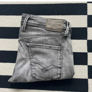 Replay Anbass grå jeans - Snygga grå jeans från Replay i storlek 33/34, modell Anbass. Klassisk femficksdesign med Replay-logga på bakfickan och läderpatch i midjan. Jeansen har en modern passform och är perfekta för en stilren vardagslook.