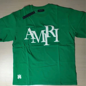 Grön t-shirt från Amiri med stor logga - Snygg grön t-shirt från Amiri med stor vit logotyp framtill. Klassisk rund halsringning och lite oversize passform. Perfekt för dig som vill sticka ut med en exklusiv streetwear-look.