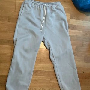 Ljusgrå mjukisbyxor från SUMWON - Ljusgrå mjukisbyxor från SUMWON med elastisk midja och vit dragsko. Byxorna har en avslappnad passform och är tillverkade i mjukt material, perfekta för chill dagar eller träning.