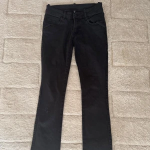 Svarta jeansbyxor med bootcut - Svarta bootcut jeans. Köpta secondhand. Baksidan har två fickor med lock och knappdetalj. Ber om ursäkt för lite dammig bild, byxorna tvättas innan dom postas 