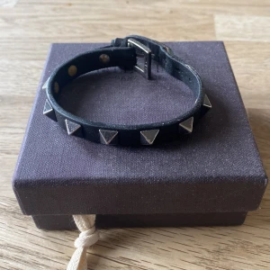 Svart armband med nitar från Valentino - Tror inte mina ögon någonsin skådat nått så grisch. Otroligt stilren och passar precis till allt. Dejt med någons dotter vars far äger en bilfirma (hon har det bra ställt)? Flexa lite på uteliggaren utanför Coop? Gå till skolan och skryta inför den grabben med Arigatos på sig (det är 2025 komigen steppa upp)? Denna passar till allt. Finns en liten skada på ena sidan, syns inte när man har på sig och går säkert att limma ihop. Nypris typ 3 larre.
