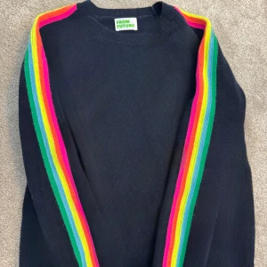 Mörkblå stickad tröja From Future  - Mörkblå stickad tröja från From Future i storlek S. Tröjan har långa ärmar med färgglada ränder i regnbågens färger. Perfekt för dig som vill ha en färgklick i garderoben!