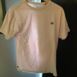 Ljusrosa t-shirt från Vans - Säljer en ljusrosa t-shirt från Vans med diskret mönster och klassisk Vans-logga på bröstet. T-shirten är i mjuk bomull och har en avslappnad passform med korta ärmar. Perfekt för en chill och stilren look.