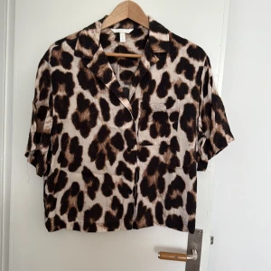 Leopardmönstrad resortskjorta i viskos från HM - Kortärmad resortskjorta i viskos från HM med leopardmönster i svart och brunt på beige botten. Skjortan har klassisk krage, knappar framtill och en bröstficka. Lätt boxig modell. 