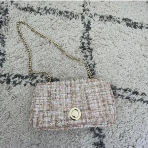 Rosa/Beige rutig axelväska med kedja - Säljer en rosa/ beige axelväska med rutigt mönster och snygg guldfärgad kedja. Väskan har ett stilrent spänne framtill och är gjord i ett tygmaterial som påminner om tweed. Perfekt för dig som gillar klassisk men trendig stil.