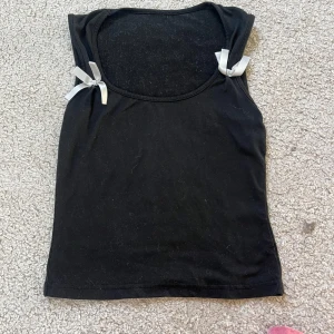 Svart linnetopp med rosetter. Säljer flera toppar från shein för 15 kr st.  - En svart ärmlös linnetopp med rund halsringning och två söta vita rosetter på axlarna. 