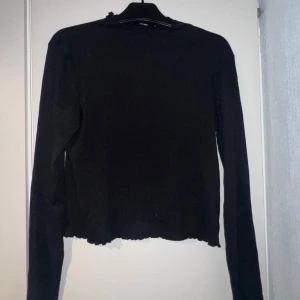 Svart ribbad långärmad tröja BikBok - Svart långärmad tröja från BikBok i ribbat material. Tröjan har en tight passform, vågig kant vid hals, ärmslut och nederkant för en extra detalj. Perfekt att styla med jeans eller kjol för en clean look. Aldrig använd. Skulle passa M-L