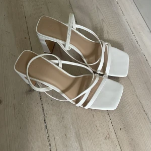klackskor - Snygga vita klackskor från H&M med fyrkantig tå och smala remmar. Skorna har en stabil hög klack och öppen tå, perfekt till sommarens outfits. Tillverkade i syntetmaterial med stilren design och trendig look.