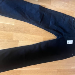 Svarta jeans från 157, storlek 32/30 - Svarta klassiska jeans från 157 med raka ben och femficksmodell. Jeansen har normal passform och är tillverkade i bomull med en snygg matt finish. Perfekta för dig som gillar stilrena och enkla basplagg. Märkta med etikett och har knapp- och dragkedjestängning.