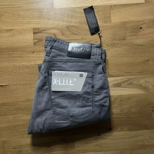 Replay Anbass grå jeans X-Lite+ - Säljer ett par grå Replay Anbass jeans i X-Lite+ ultra light denim. De har klassisk femficksdesign, normal passform och raka ben. Snygg Replay-logga på bakfickan och läderpatch i midjan. Perfekta för dig som gillar stilrena och bekväma jeans.