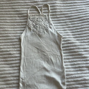 Vit ribbad linnetopp från Hollister XS - Supersöt vit ribbad linnetopp från Hollister med tunna axelband och spetsdetalj framtill. Toppen har en tight passform och är perfekt för varma dagar. Metallbricka med Hollister-logga nertill ger en extra touch. Från Must-Have Collection. Har två fläckar, en på baksidan och en vid logan nertill, men de syns knappt!