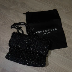 Väska Kurt Geiger - Säljer denna superfina Kurt Geiger väska som är i bra skick. Den är svart med paljetter. Har fått många komplimanger pga denna väska. Den kostar som ny med bra pris 2200kr men säljer endast för 1499kr. Den har en repa på örnen men märks inte av. Kontakta mig vid frågor eller funderingar!