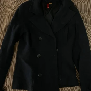 Blå skepparkavaj med knappar - Klassisk blånskepparkavaj med dubbelknäppning och bred krage. Jackan har en stilren look med fyra stora knappar framtill och är helfodrad. Perfekt för dig som gillar tidlös och clean stil. har en liten fläck på kragen (syns på bilden), kan eventuellt gå att skrubba bort samt saknar knappen högst upp på ena sidan, inget som märks dock då man bara kan andvända knapparna på andra sidan istället 😇