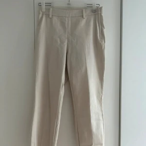 Ljusbeige byxa/slacks - Snygga ljusbeige byxor från H&M med slim passform och hög midja. Byxorna har bälteshällor, två bakfickor och är tillverkade i ett mjukt bomullsmaterial med lite stretch. Perfekta för en clean och stilren look. Dragkedjan är på sidan
