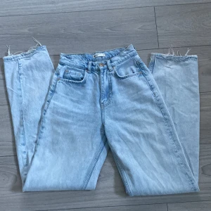 Ljusblå high waist jeans från Gina Tricot - Säljer ett par ljusblå high waist jeans från Gina Tricot, modell Perfect Jeans. Jeansen har raka ben med råa och slitna benslut samt slitningar på bakfickan. Jeansen är i mjuk denim och har en avslappnad vibe.