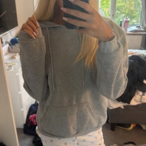 Grå hoodie med svart tryck bak - Säljer en grå hoodie med stor huva och snörning. På ryggen finns ett svart tryck med coola grafiska ansikten i seriestil. Perfekt för chill dagar eller när du vill ha en avslappnad look. 💓