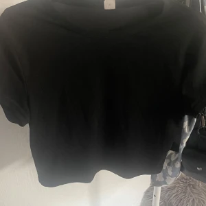 Svart croppad topp från SHEIN Teen - Enkel svart croppad topp från SHEIN Teen med korta ärmar och rund hals. T-shirten är i mjuk bomull och passar perfekt till jeans eller kjol för en clean och stilren look.