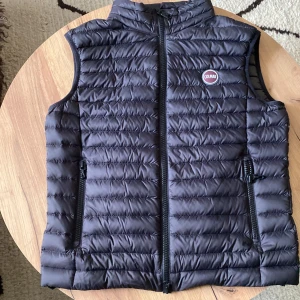 Svart väst från Colmar - Snygg svart väst från Colmar med quiltad design och hög krage. Västen har två dragkedjefickor framtill och en tydlig Colmar-logga på bröstet. Perfekt att slänga över en hoodie för extra värme. Materialet är lätt och smidigt syntet. Aldrig använd pågrund av fel storlek.