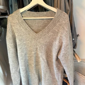 Grå stickad v-ringad tröja Gina Tricot - Mysig grå stickad tröja från Gina Tricot med v-ringning och ribbade muddar. Perfekt för lager-på-lager och chill dagar. Enkel att matcha med jeans eller kjol för en avslappnad look. Har aldrig använts! 