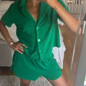 Gröna frottéshorts med resår + frottepike - Snygga gröna shorts i mjuk frotté med elastisk midja för skön passform. Grön piké som följer med. Perfekta för varma dagar och chill hemma. De har en loose fit och är riktigt bekväma att bära. Färgen är klargrön och materialet känns svalt mot huden.
