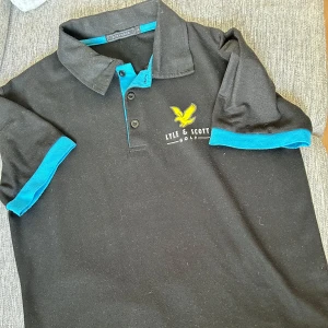 Lyle & scott piké  - Säljer en stilren svart golfpiké från klassiska Lyle & Scott – perfekt både på golfbanan och till vardags. Tröjan har en modern passform, bekvämt funktionsmaterial som andas, samt den ikoniska örn-loggan broderad på bröstet. En mångsidig piké som funkar lika bra till chinos som till golfshorts.