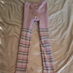 Rosa randiga långa strumpor (barn) - Mysiga långa strumpor i ljusrosa med horisontella ränder i grått, vitt och beige. Perfekta för att hålla värmen hemma eller under kalla dagar. Mjukt material som känns skönt mot huden och ger en avslappnad vibe. Barn storlek.