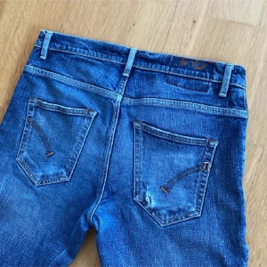 Blå dondup jeans - Säljer ett par blå dondup jeans i storlek 31. Jeansen har slitna detaljer och hål på knäna för en cool, avslappnad look. Klassisk femficksmodell med normal passform och något tapered ben. Tillverkade i mjukt jeansmaterial.