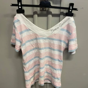 Dolce & Gabbana off-soulder topp - Superfin offshoulder topp från Dolce & Gabbana med bred vit krage och glittrande logga i strass. Toppens tyg har pastellrosa, ljusblå och vita ränder. Storlek L men passar och S. #dolcegabbana #offshoulder #sommar #sommartopp #randig #glitter #paljetter #tshirt #y2k #preppy 