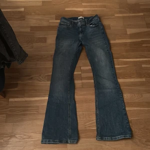 Blå bootcut jeans med utsvängda ben low waist - Säljer ett par klassiska blå jeans med bootcut och utsvängda ben. Jeansen har fem fickor, normal midja och snygg tvättad look. Perfekta för dig som gillar retrostil och vill ha ett par jeans som sticker ut lite extra.