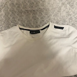 Vit t-shirt från Sail Racing XS - Vit t-shirt från Sail Racing i klassisk modell med rund hals och diskret logga på axeln. Tillverkad i mjuk bomull som känns skön mot huden. Perfekt basic-plagg med stilren look och snygga detaljer på ryggen.