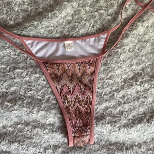 Mönstrad bikiniunderdel i rosa - Säljer en snygg bikiniunderdel i storlek S. Den har ett unikt mönster i rosa och beige toner med smala band i sidorna. Materialet är 100% polyester. Aldrig använd. 