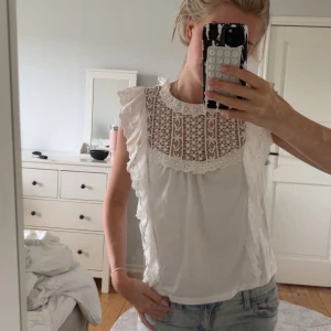 Vit blus med spets och volang - Superfin vit blus med broderad spets upptill och volangdetaljer längs axlarna. Hög halsringning och ärmlös design ger en romantisk vibe. Andvänd några enstaka gånger!💓💓