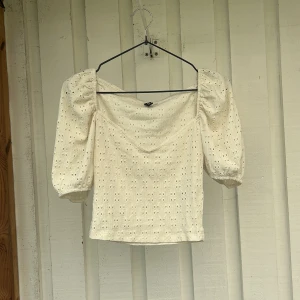 Vit blus med puffärm och broderi - Superfin vit blus med puffiga korta ärmar och broderade hålmönster. Toppen har en lätt croppad passform och fyrkantig ringning. Perfekt för dig som gillar romantiska detaljer och somriga vibes.