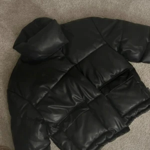 Svart pufferjacka från Missguided - Säljer en svart pufferjacka från Missguided med oversized passform. Jackan har stora fickor framtill, hög krage och snörning i nederkant. Materialet är syntet med en glansig finish. Använd cirka 4 gånger, nyskick. 