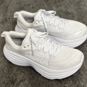 Hoka Bondi 8 - Hoka Bondi 8 i helt vitt, dammodell i storlek 37 1/3 (US 6 B). Skorna är i bra skick.  Nyimpregnerade hos Stadium med smuts- och vattenavvisande medel – en behandling som skyddar skorna och förlänger livslängden. Originalinnersulan är helt ny och oanvänd – jag använde egna inlägg.   Skorna är försiktigt rengjorda för hand. Mindre slitage på yttersulan, men inget som påverkar komfort eller funktion.