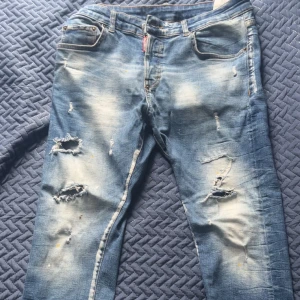 Dsquared2 slitna blå jeans slim fit - Riktigt snygga blå jeans från Dsquared2 med slitna detaljer och trasiga partier framtill. Slim fit-modell med klassisk femficksdesign och ljusa tvättade partier. Tillverkade i Italien av jeansmaterial. Perfekta för dig som gillar en edgy streetstil.
