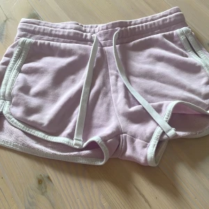 Ljusrosa mjuka shorts med snörning - Supermjuka ljusrosa shorts med vita kanter och snörning i midjan. Perfekta för sommardagar eller chill hemma. De har en sportig vibe och är gjorda i bomullsmaterial som känns skönt mot huden. Säljer dessa shorts för dem är alldeles för små för mig😊