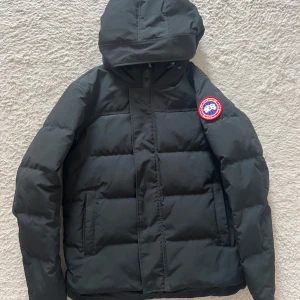 Canada Goose Macmillan - Säljer en svart dunjacka från Canada Goose med huva och klassisk logga på ärmen. Jackan är quiltad och har dragkedja framtill samt två fickor. Perfekt för kalla dagar och riktigt snygg streetstil.   Mycket välkomna att skicka frågor om vad som helst👍😁