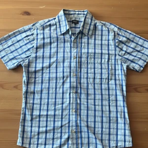 Blårutig kortärmad skjorta från Max - Kortärmad skjorta från Max i blått och vitt rutigt mönster. Skjortan har klassisk krage, bröstficka och knäppning framtill. Perfekt för varma dagar och chill stil. Tillverkad i lätt bomullsmaterial som andas.