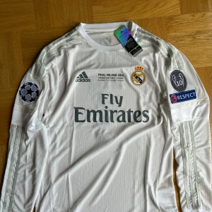 Real Madrid Finaltröja Ronaldo 2016 - Real Madrid långärmad fotbollströja från Champions League-finalen 2016, med Ronaldo 7 på ryggen. Vit med silverdetaljer, klubbmärke, Adidas-logga och Fly Emirates-tryck. Patchar på ärmarna och autentisk Adizero-label. Tillverkad i lätt, ventilerande material.