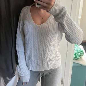 Vit Hollister tröja  - Vit kabelstickad tröja från Hollister med v-ringning och långa ärmar. Tröjan har en liten broderad logga på bröstet och breda muddar vid ärmslut och nederkant. Perfekt för lager-på-lager och chill dagar💗