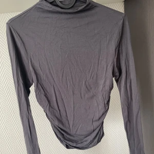 Mörkgrå polotröja i tunn bomull - En stilren mörkgrå polotröja med lång ärm i tunn och mjuk bomull. Tröjan har en klassisk polokrage och sitter snyggt mot kroppen.