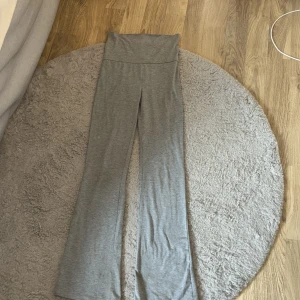 Grå bootcut yoga pants från Gina Tricot - Grå yoga pants från Gina Tricot med bootcut-ben och låg midja. Byxorna är i mjukt och stretchigt material, perfekta för en chill och avslappnad stil. Snygg passform som sitter skönt över höfterna och släpper ut vid benen.